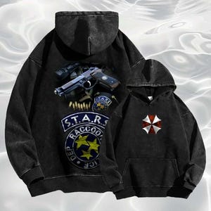 May include: Two black hooded sweatshirts. One features a graphic of a gun, grenades, and the text "S.T.A.R.S. Raccoon Dep. Police". The other has a red and white umbrella logo.