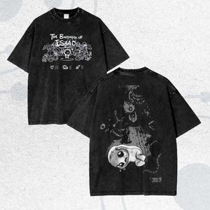 Könnte beinhalten: Schwarzes, übergroßes T-Shirt mit Grafiken auf Vorder- und Rückseite. Auf der Vorderseite steht der Text "The Binding of Isaac" mit Cartoon-Charakteren. Die Rückseite zeigt eine detaillierte Illustration.