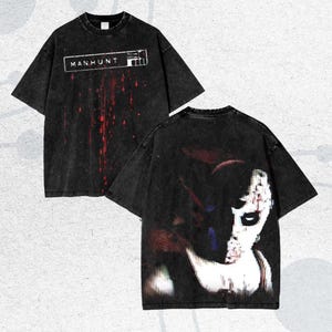May include: Black, oversized t-shirts with a distressed, vintage look. The front features the text "MANHUNT" in a white rectangle with red splatter. The back displays a distorted graphic of a face with red and blue accents.