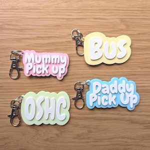 Può includere: Quattro portachiavi colorati con chiusure argentate. I portachiavi hanno la forma di fumetti e riportano le scritte: "Mummy Pick up", "Bus", "OSHC" e "Daddy Pick Up". I portachiavi sono rosa, gialli, verde chiaro e blu.