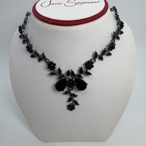 Pu&ograve; includere: Una collana floreale nera con pendenti a goccia. La collana &egrave; esposta su un busto bianco. La collana ha un design delicato con piccoli fiori e foglie. Il marchio "Jane Seymour" &egrave; visibile in alto.