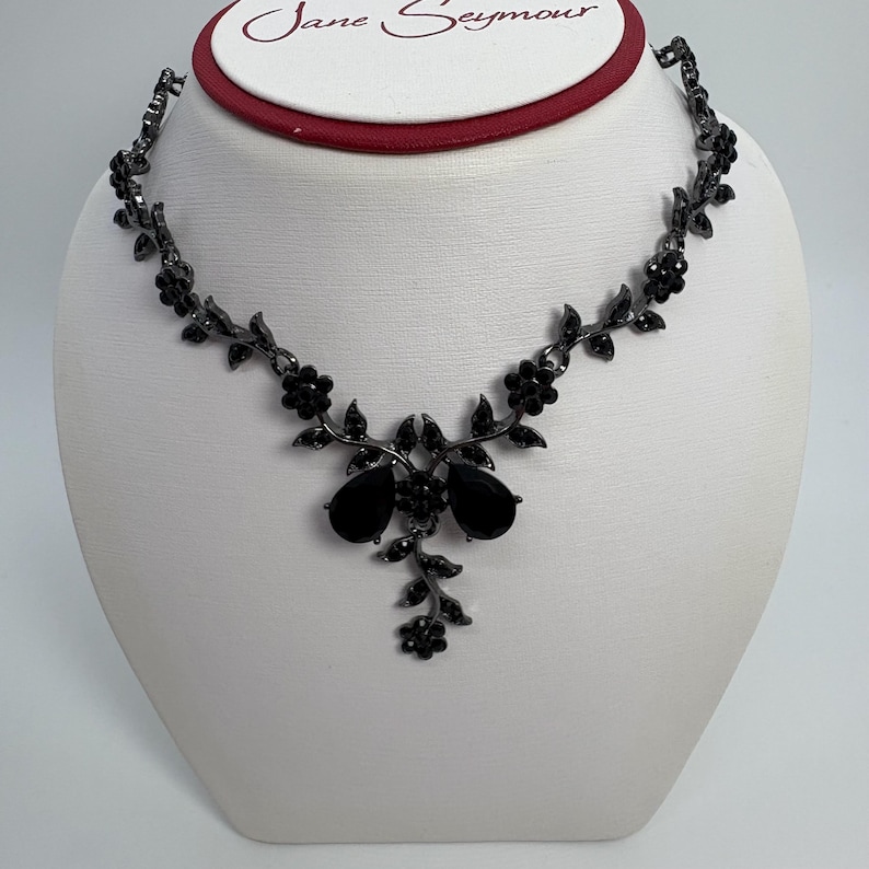 Pu&ograve; includere: Una collana floreale nera con pendenti a goccia. La collana &egrave; esposta su un busto bianco. La collana ha un design delicato con piccoli fiori e foglie. Il marchio "Jane Seymour" &egrave; visibile in alto.