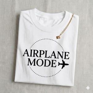 May include: White t-shirt with the words "AIRPLANE MODE" in black, encircled by a dotted line, and a small airplane graphic. A gold necklace with a square pendant rests on the shirt.