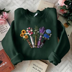 Puede incluir: Sudadera verde oscuro con un dise&ntilde;o floral bordado. El bordado presenta girasoles, rosas, lavanda y flores azules dispuestas en un patr&oacute;n similar a un jarr&oacute;n. La sudadera est&aacute; hecha de un material suave y es perfecta para uso casual.