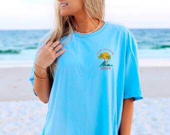 May include: A light blue t-shirt with a graphic of a palm tree and the text "If your vibe isn't everything, beach".