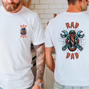 以下が含まれることがあります： 白いTシャツで、背面に蛇とレンチのグラフィックと「Rad Dad」の文字が書かれています。Tシャツの前面には、蛇のグラフィックの小さいバージョンと「Rad Dad」の文字が書かれています。