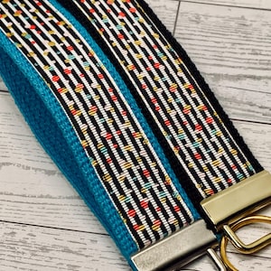 May include: Close-up of two key fobs. One is turquoise blue, and the other is black. Both have a black and white striped pattern with colorful dots. The key fobs have metal hardware and key rings.