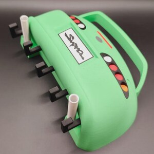 May include: A light green device with a handle, the word "Supra" on a white rectangle, and several black and white components. It has a series of colored lights and a handle. The device has a unique design.