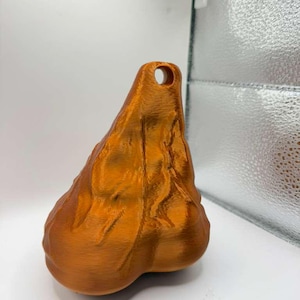 May include: A metallic copper-colored, three-dimensional object with a textured, organic, and irregular shape. The object features a prominent, rounded base that tapers upward to a narrow point, which contains a single, circular hole for hanging.