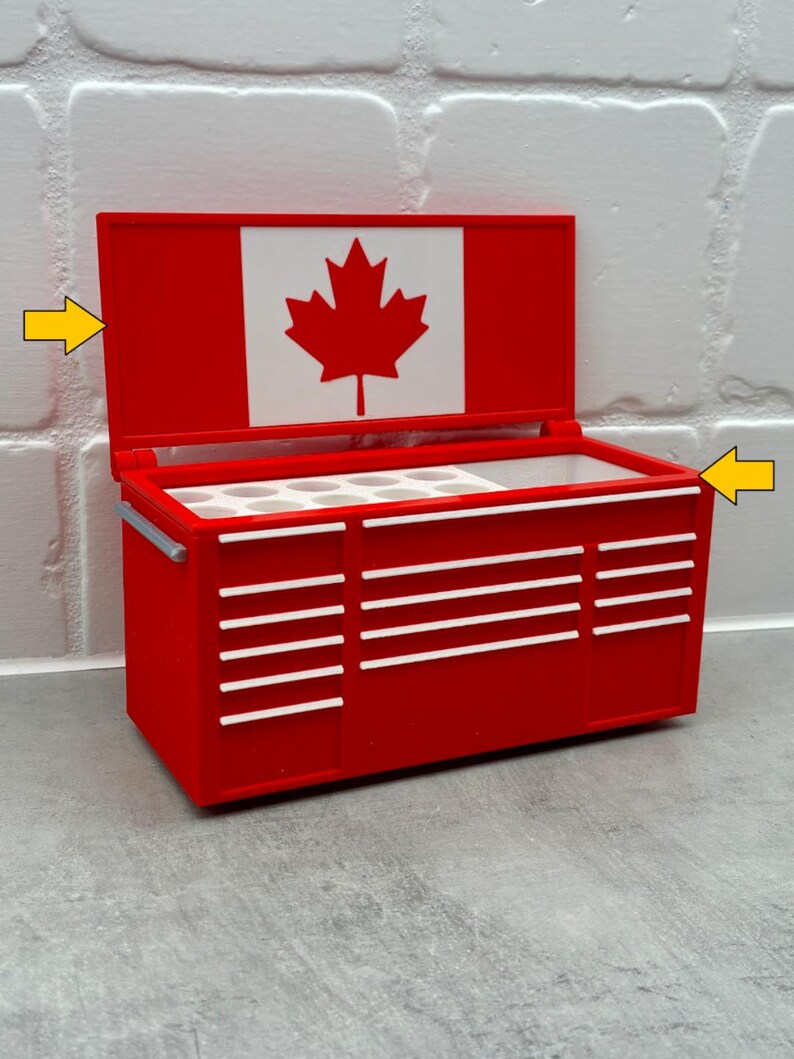 May include: A red toolbox with white accents and a Canadian flag on the lid. The toolbox has multiple drawers and a handle. The lid is open, revealing the interior. The toolbox is sitting on a gray surface.