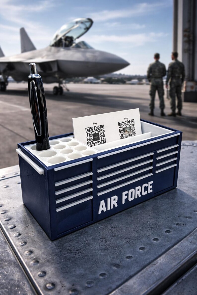 May include: A navy blue desk organizer with the words "AIR FORCE" in white. The organizer has a pen holder, a slot for business cards, and a black pen. A military jet is in the background.