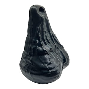 May include: A black, three-dimensional, teardrop-shaped object with a glossy, uneven, and textured surface. The top of the object features a small, circular hole, and the overall form is characterized by organic, flowing ridges and contours.
