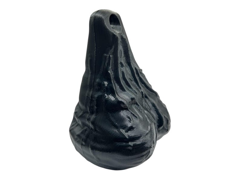 May include: A black, three-dimensional, teardrop-shaped object with a glossy, uneven, and textured surface. The top of the object features a small, circular hole, and the overall form is characterized by organic, flowing ridges and contours.