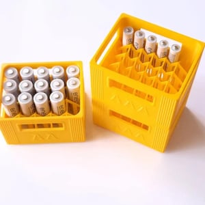 May include: Two yellow plastic battery storage crates filled with AA batteries. One crate is full, and the other is partially filled. The batteries are silver and white with black text. The crates are on a white surface.