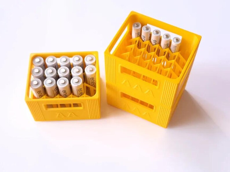 May include: Two yellow plastic battery storage crates filled with AA batteries. One crate is full, and the other is partially filled. The batteries are silver and white with black text. The crates are on a white surface.