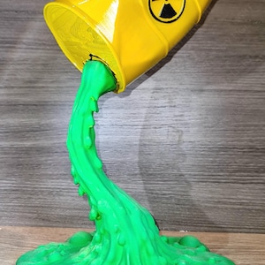 May include: A yellow barrel with a black radiation symbol is tilted, pouring out a stream of bright green liquid. The liquid pools on the surface, creating a unique decorative piece.