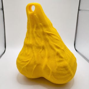 May include: A bright yellow, three-dimensional object with a textured, organic surface featuring prominent vein-like ridges and a rounded, bulbous shape. The top section tapers to a point and includes a circular hole for hanging or attachment.