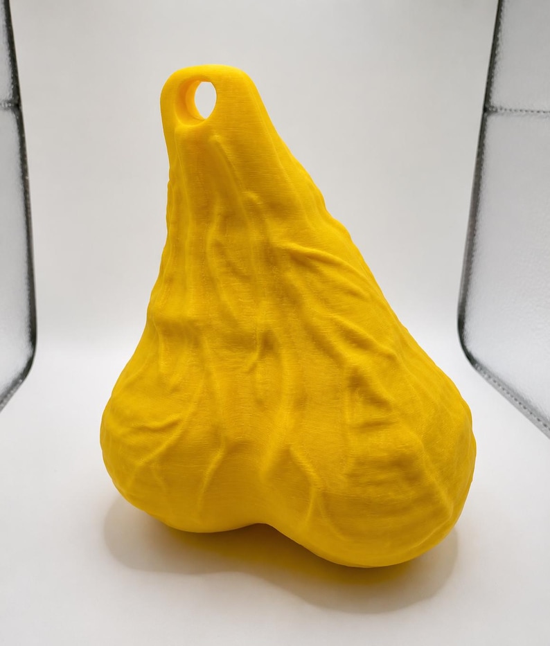 May include: A bright yellow, three-dimensional object with a textured, organic surface featuring prominent vein-like ridges and a rounded, bulbous shape. The top section tapers to a point and includes a circular hole for hanging or attachment.