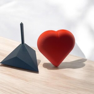 Pu&ograve; includere: Un oggetto rosso a forma di cuore e un oggetto triangolare nero con una punta appuntita. Entrambi gli oggetti sono fatti di un materiale testurizzato.