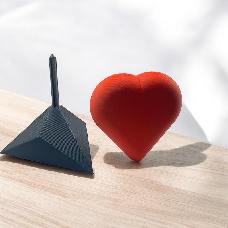 Pu&ograve; includere: Un oggetto rosso a forma di cuore e un oggetto triangolare nero con una punta appuntita. Entrambi gli oggetti sono fatti di un materiale testurizzato.