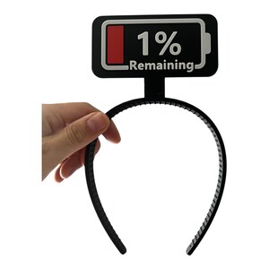 May include: Black headband with a battery icon that reads "1% Remaining." The battery icon is black with a red bar and white text. The headband is held by a hand.