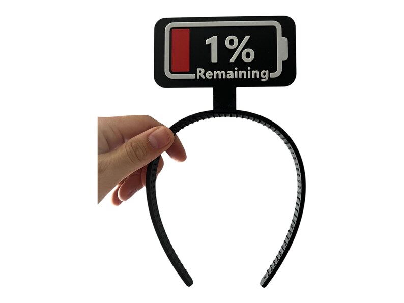 May include: Black headband with a battery icon that reads "1% Remaining." The battery icon is black with a red bar and white text. The headband is held by a hand.