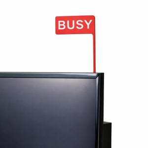 Könnte beinhalten: Ein rotes Schild mit dem weißen Wort "BUSY" ist an der Oberseite eines schwarzen Fernsehers befestigt. Das Schild ist rechteckig und hat einen dünnen, roten Stiel.