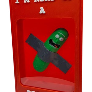 May include: A red framed display featuring a green pickle character with a gray weapon. The text "I'M KIND OF A" is at the top, and "BIG DILL" is at the bottom in white letters. The pickle has a smiling face.