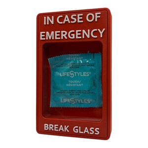 May include: A red plastic box with the words "IN CASE OF EMERGENCY" and "BREAK GLASS" in white. Inside the box is a blue and white Lifestyles condom packet. The packet reads "TOUGH/RESISTANT".