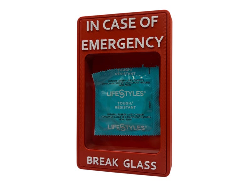 May include: A red plastic box with the words "IN CASE OF EMERGENCY" and "BREAK GLASS" in white. Inside the box is a blue and white Lifestyles condom packet. The packet reads "TOUGH/RESISTANT".