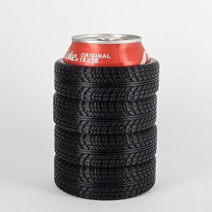 May include: A black tire-shaped can cooler with five stacked tires. The cooler is holding a red can of Coca-Cola with the text "Original Taste" on it.