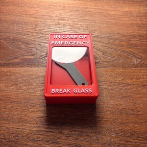 May include: Red break glass box with the text "IN CASE OF EMERGENCY" and "BREAK GLASS" in white lettering. A small metal tool is visible inside the box.