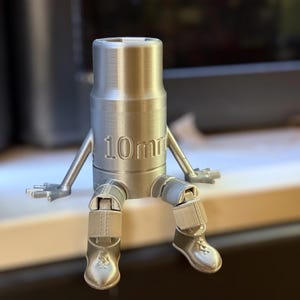 May include: A silver 3D printed figurine of a person holding a 10mm socket wrench. The figurine has articulated arms and legs and is sitting down.