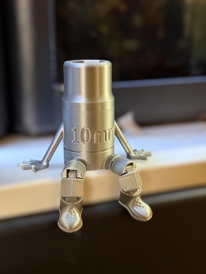 May include: A silver 3D printed figurine of a person holding a 10mm socket wrench. The figurine has articulated arms and legs and is sitting down.