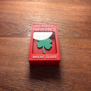 May include: Red break glass box with the text "IN CASE OF EMERGENCY" and "BREAK GLASS" in white lettering. A green four-leaf clover is visible inside the box.