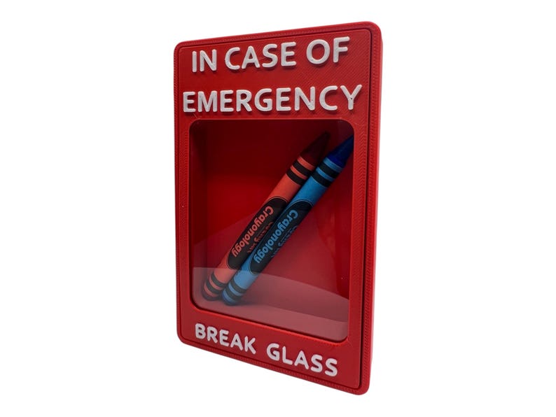 May include: A rectangular red wall-mounted display case with a clear front panel. The text IN CASE OF EMERGENCY is at the top and BREAK GLASS is at the bottom in white letters. Inside the case are two Crayonology crayons, one red and one blue.