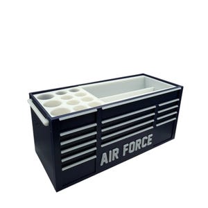 Op de afbeelding: Een marineblauwe gereedschapskist met witte accenten en de woorden "AIR FORCE" in het wit. De kist heeft meerdere laden en compartimenten, waaronder ronde houders. Het heeft een wit interieur en een handvat aan de zijkant.