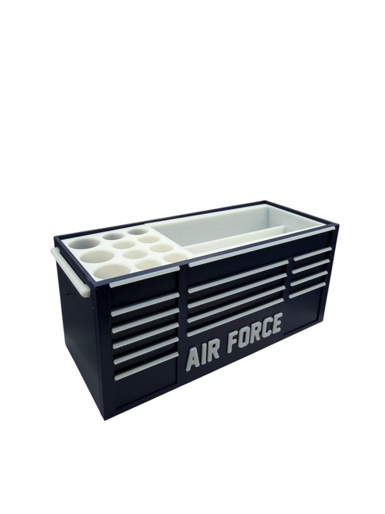Op de afbeelding: Een marineblauwe gereedschapskist met witte accenten en de woorden "AIR FORCE" in het wit. De kist heeft meerdere laden en compartimenten, waaronder ronde houders. Het heeft een wit interieur en een handvat aan de zijkant.