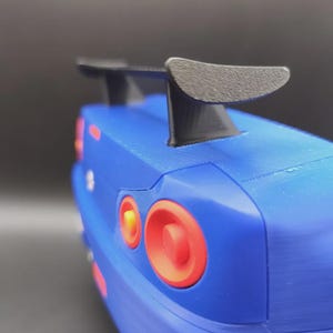 May include: A blue toy car with a black spoiler. The car has red and orange taillights. The image is a close-up of the rear of the car.