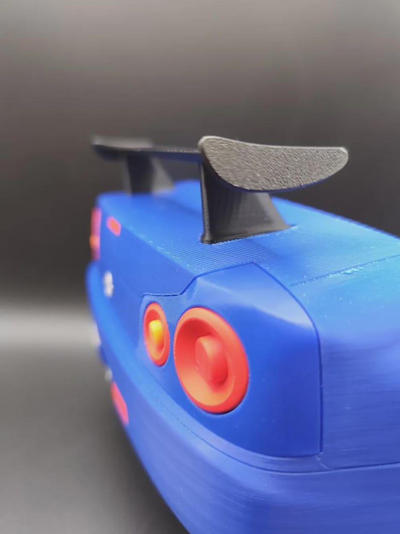 May include: A blue toy car with a black spoiler. The car has red and orange taillights. The image is a close-up of the rear of the car.