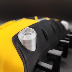 Puede incluir: Primer plano de un objeto negro y amarillo con un componente cil&iacute;ndrico plateado. El objeto tiene una superficie texturizada y una serie de protuberancias rectangulares negras. El dise&ntilde;o presenta una combinaci&oacute;n de amarillo brillante y negro, con acentos plateados.