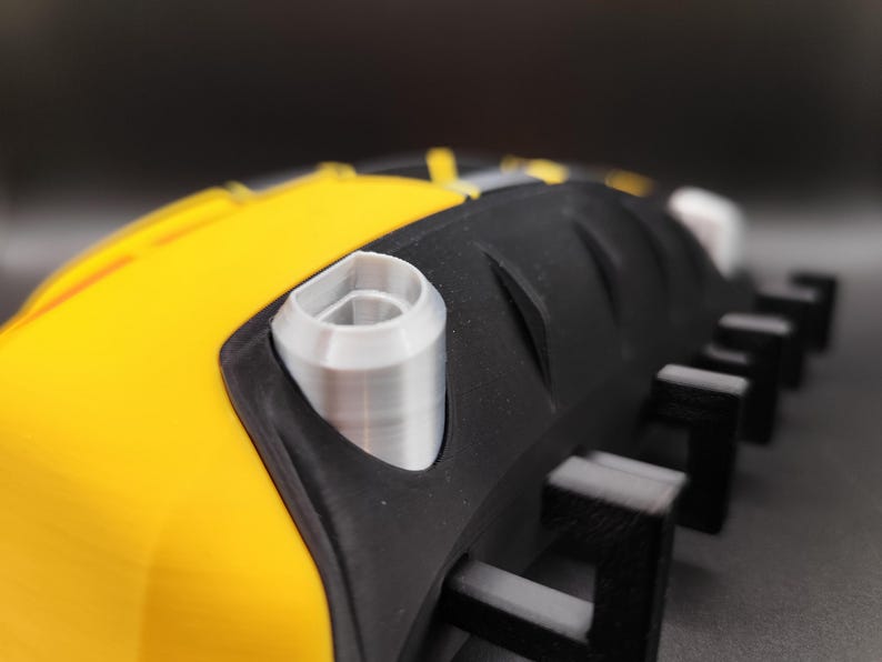 Puede incluir: Primer plano de un objeto negro y amarillo con un componente cil&iacute;ndrico plateado. El objeto tiene una superficie texturizada y una serie de protuberancias rectangulares negras. El dise&ntilde;o presenta una combinaci&oacute;n de amarillo brillante y negro, con acentos plateados.