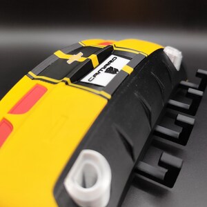 Puede incluir: Objeto amarillo y negro con forma de coche con la palabra "Camaro". El objeto tiene detalles rojos y blancos. El dise&ntilde;o es angular y moderno, con un enfoque en la est&eacute;tica automotriz.
