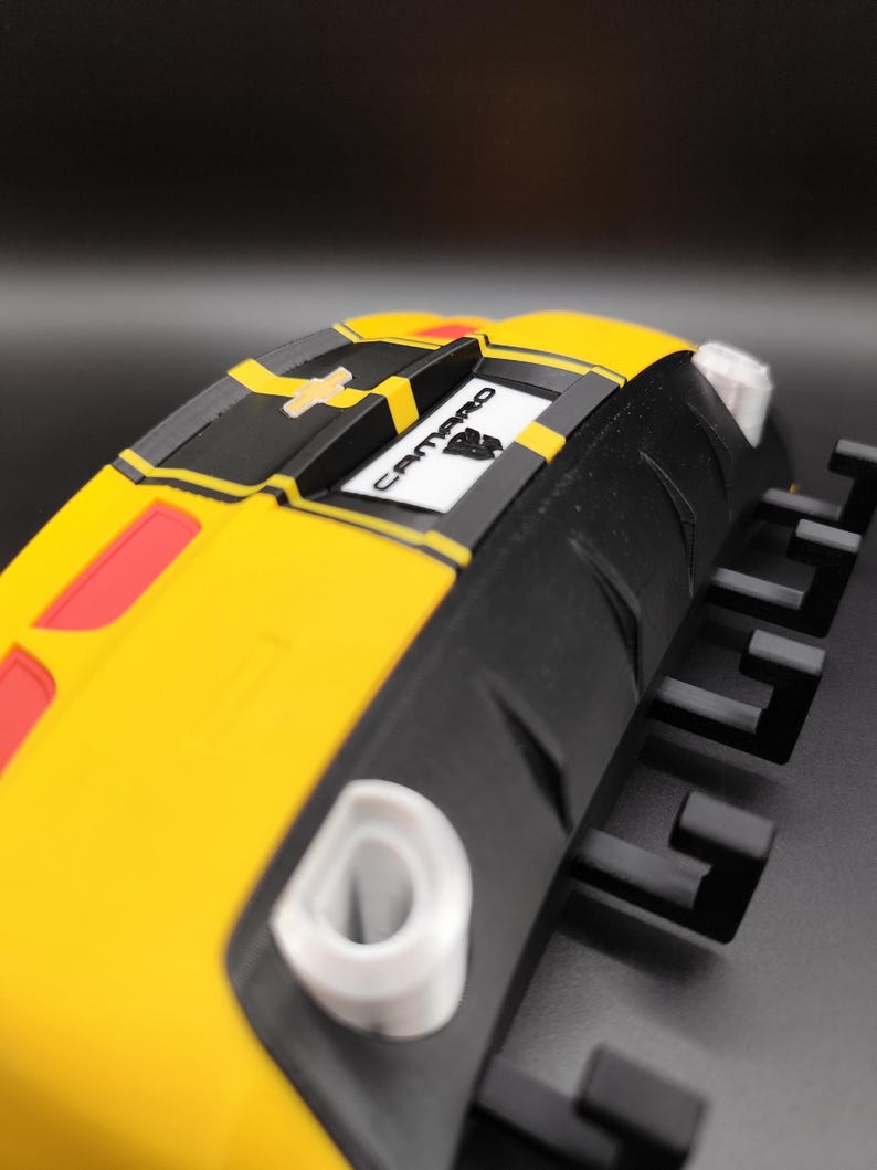 Puede incluir: Objeto amarillo y negro con forma de coche con la palabra "Camaro". El objeto tiene detalles rojos y blancos. El dise&ntilde;o es angular y moderno, con un enfoque en la est&eacute;tica automotriz.