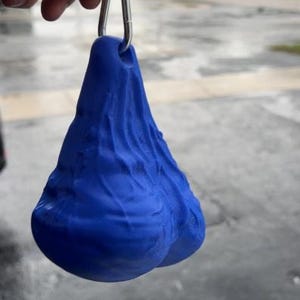 May include: A bright blue, textured, three-dimensional object with a rounded, dual-lobed shape and a wrinkled surface. The object features a small hole at the top, through which a silver-colored metal carabiner clip is attached for hanging.