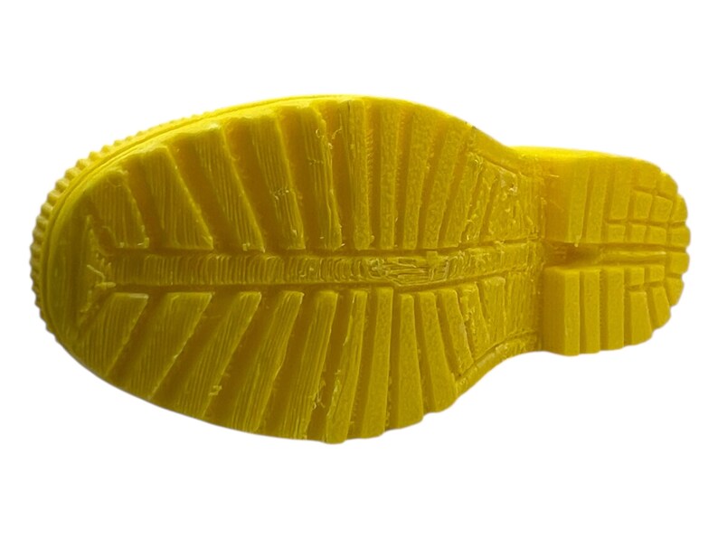 May include: A close-up of the sole of a yellow boot. The sole has a textured pattern with ridges and grooves for traction. The boot is made of a solid, bright yellow material.