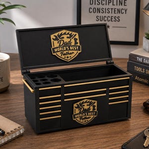 May include: Black toolbox with gold accents and the text "Dad World's Best Father." The toolbox is open, revealing an empty interior and a compartment with circular holes. A coffee mug with the text "Focus Plan Execute" is visible.