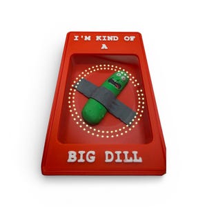 May include: A red display case with the text "I'M KIND OF A" and "BIG DILL" in white. Inside, a green pickle character with a gray strap is surrounded by a circle of lights.