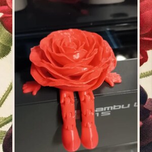 May include: A 3D printed red rose with legs. The rose is sitting on a black surface with the word "ambu" printed on it.