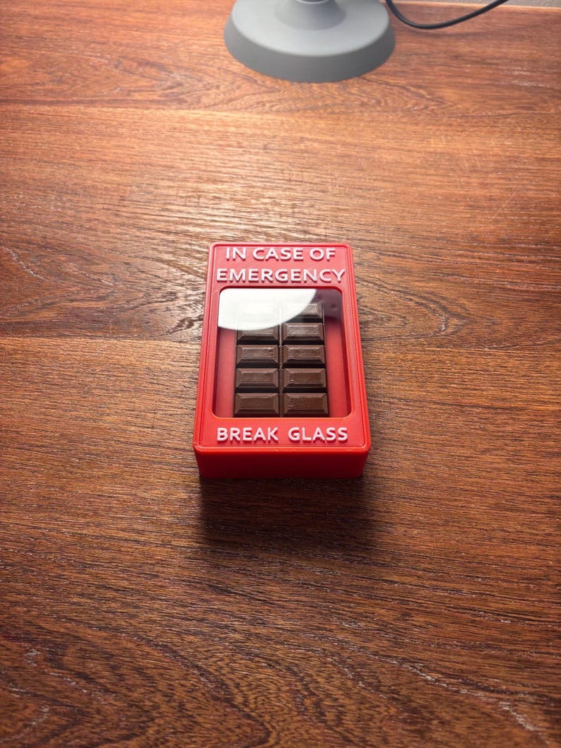 May include: A red plastic box with the text "IN CASE OF EMERGENCY" and "BREAK GLASS" on it. The box contains a chocolate bar.
